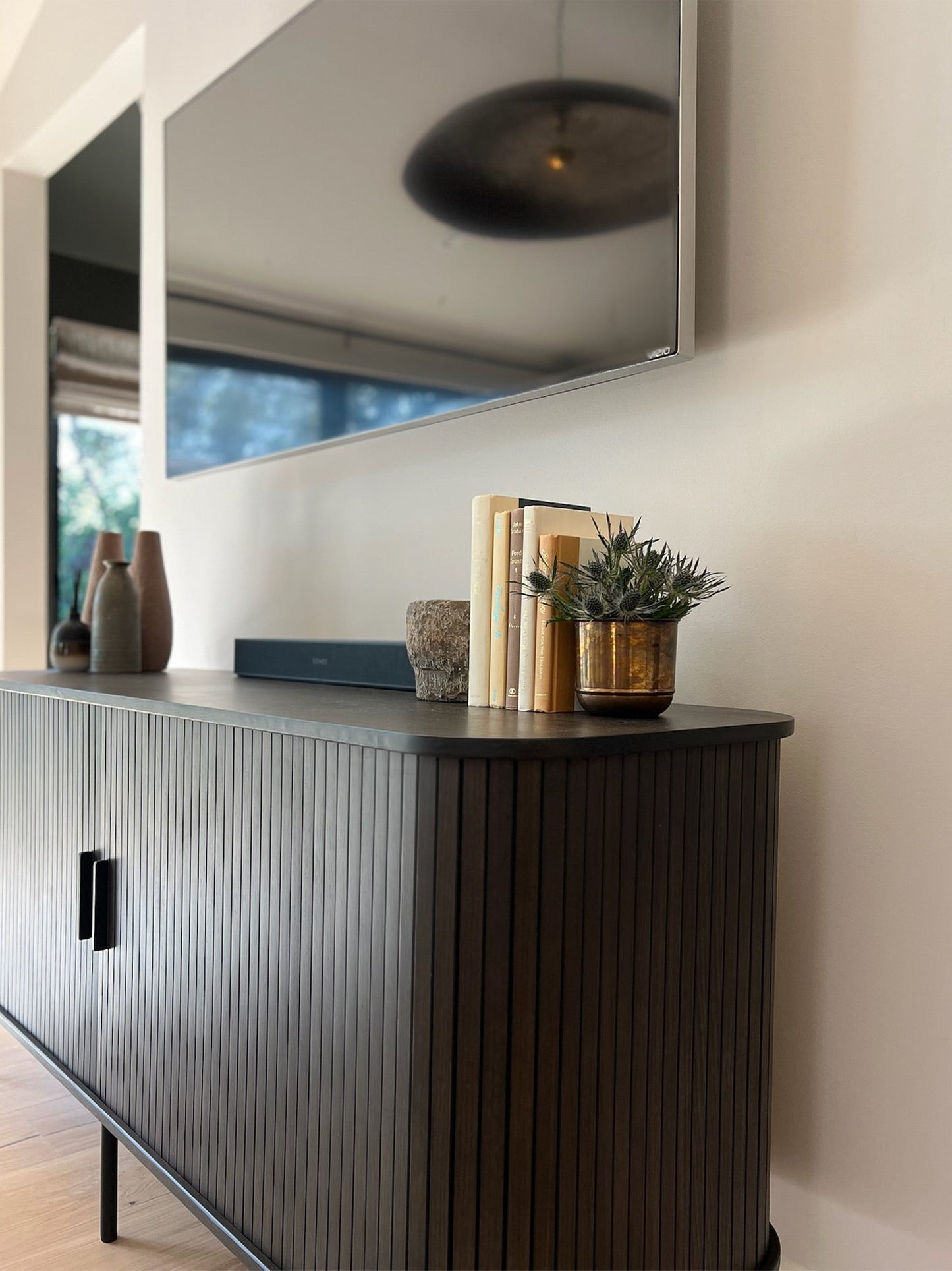 Modern interior with a dark wooden sideboard, decorative items, and a large mirror.