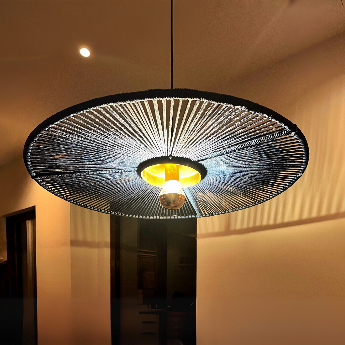 Modern pendant light with a black woven shade in a dimly lit room.