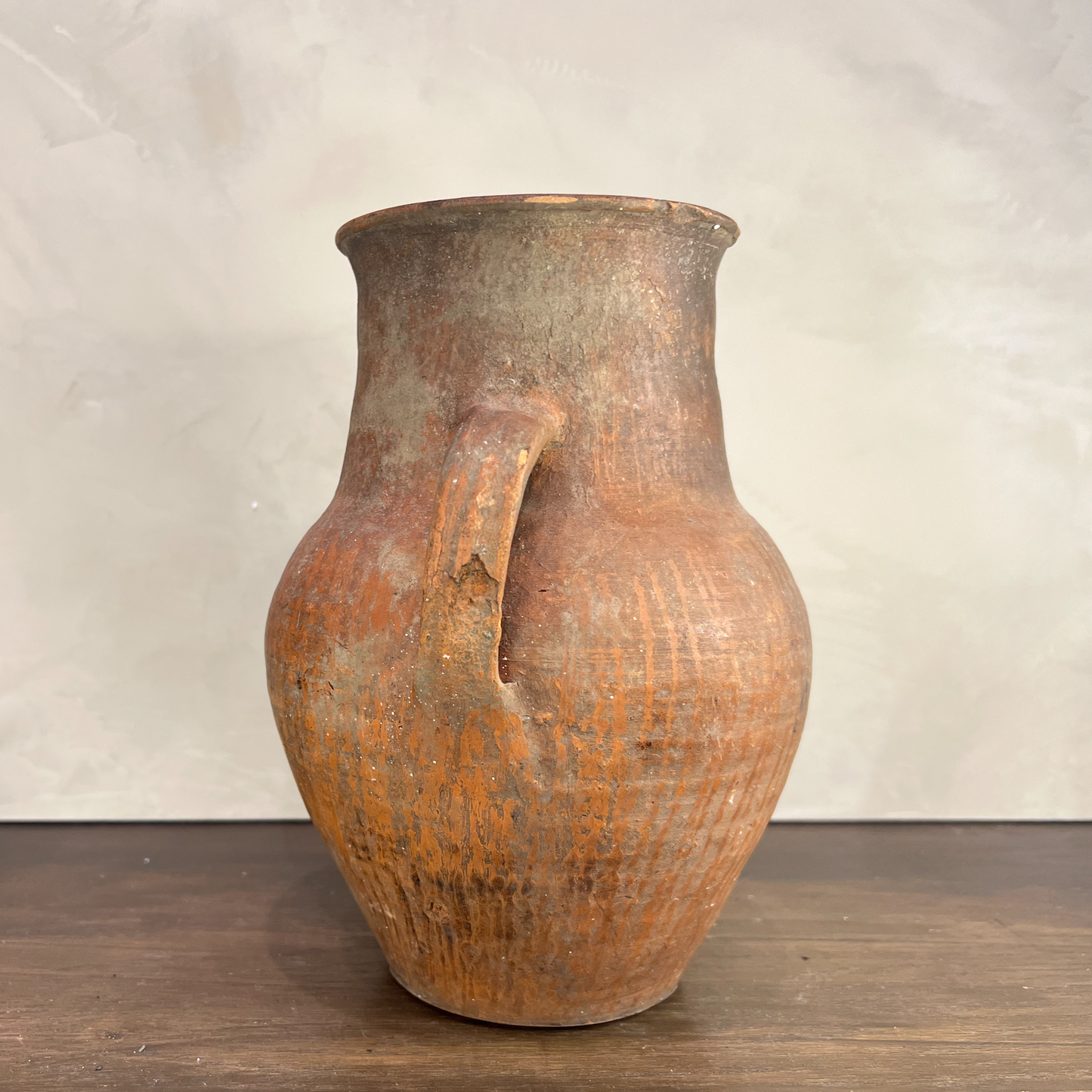 Vintage terracotta jar with a handle on a wooden surface and light gray background