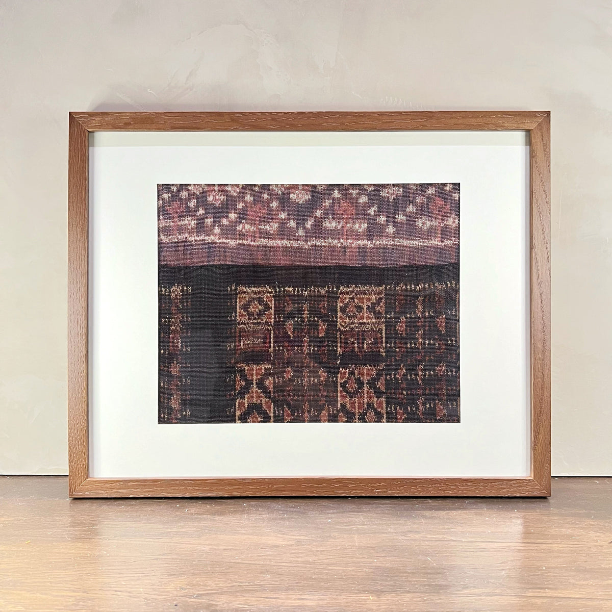 Framed textile art piece on a wooden floor with a neutral wall background
