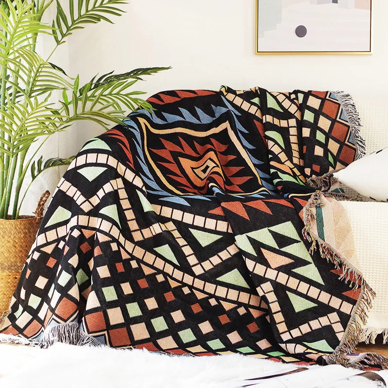Colorful patterned blanket draped over a couch with a plant in the background