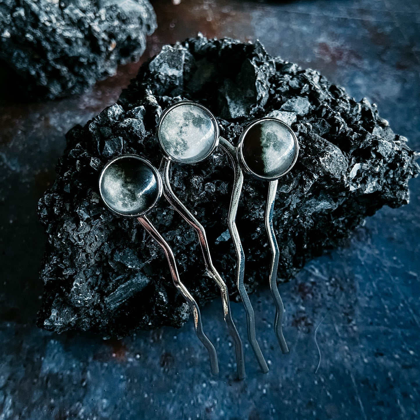 Three silver hairpins with circular ends on a dark, textured surface