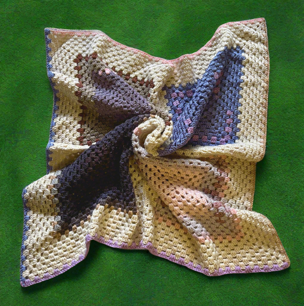 A handmade crochet afghan with a geometric pattern in red, white, and brown colors laid out on a flat surface.