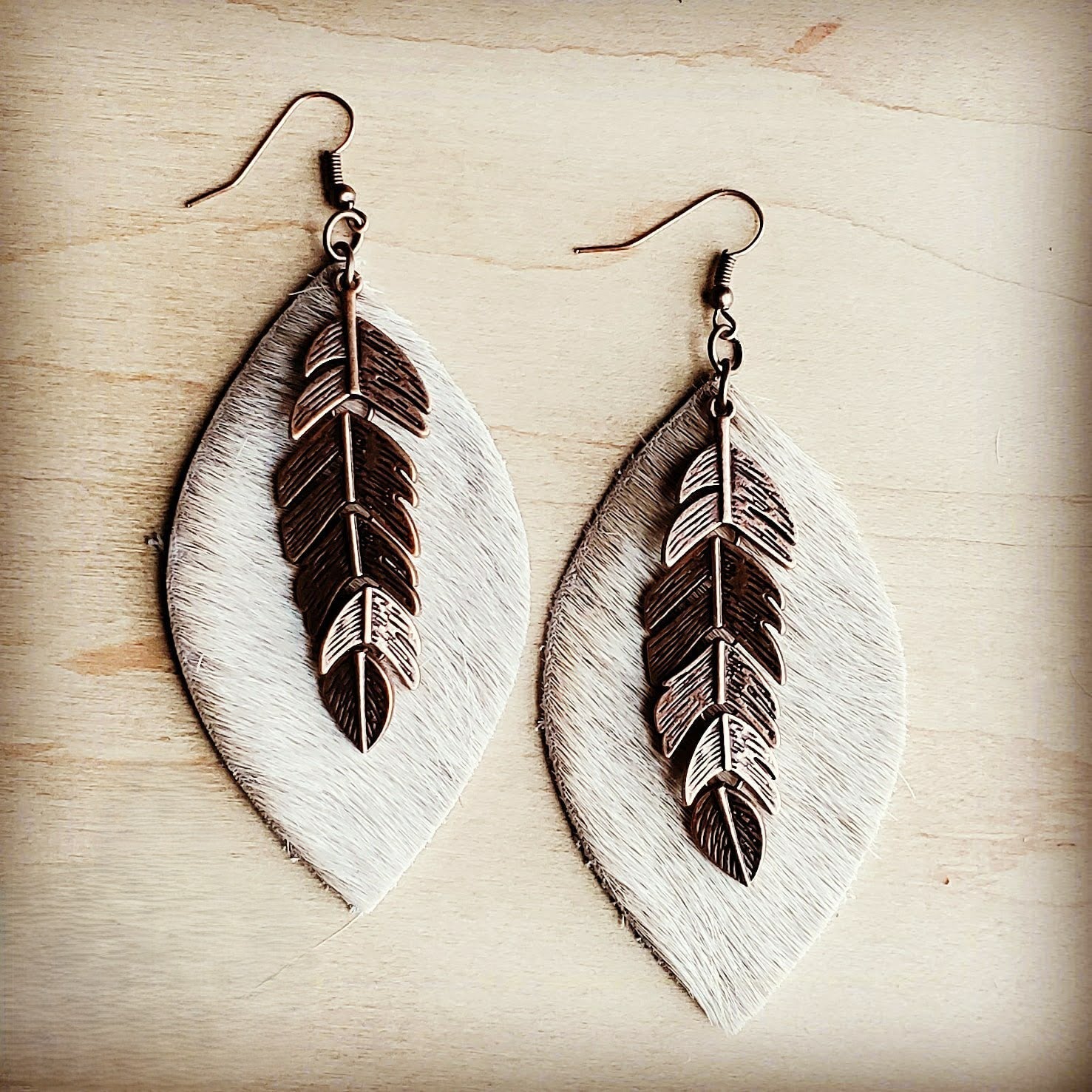 Pair of feather-shaped earrings on a wooden surface