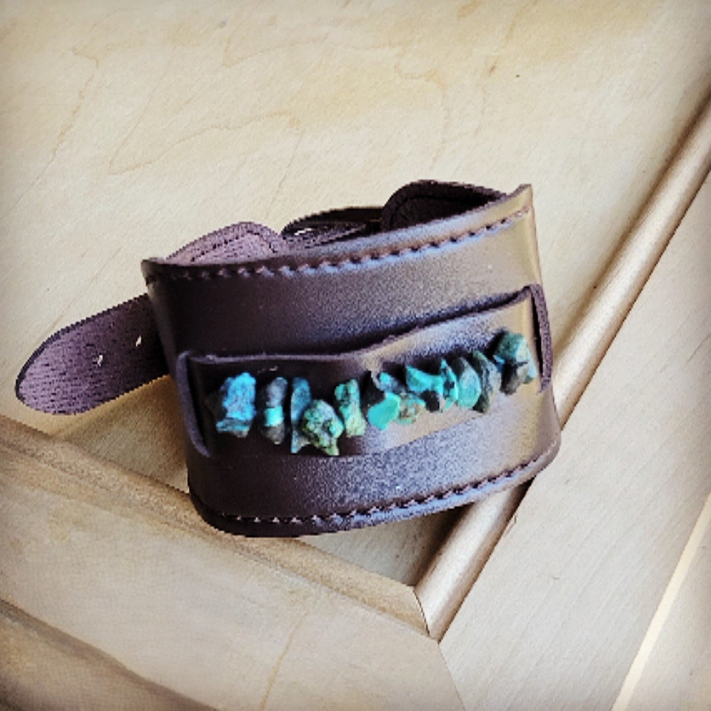 Brown leather cuff with turquoise stones on a wooden surface