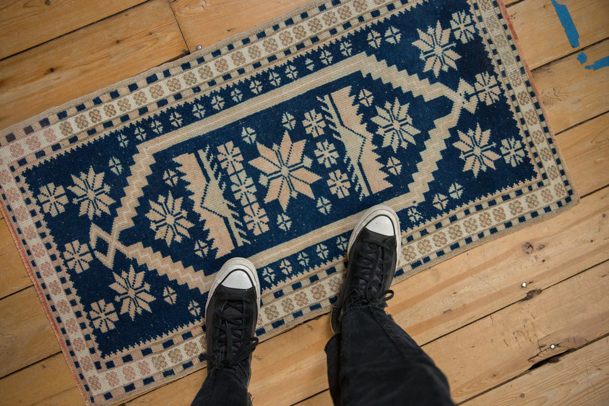 Person wearing black shoes stepping onto a blue and white patterned rug on wooden flooring