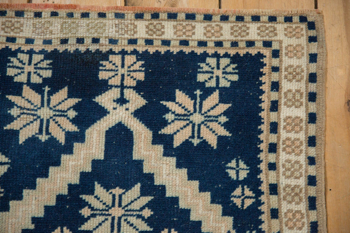 Close-up of a blue and beige patterned rug on a wooden floor.