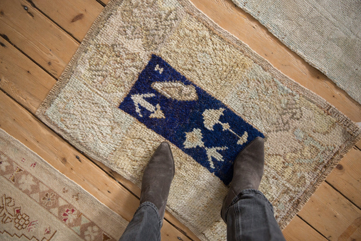 Person wearing brown shoes stepping onto a patterned rug with blue and white design on a wooden floor.