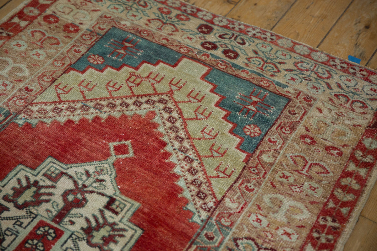 Close-up of a patterned rug with red, blue, and beige colors on a wooden floor.