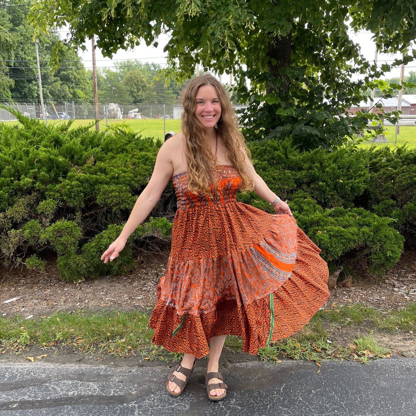 Woman in an orange dress standing outdoors with greenery in the background