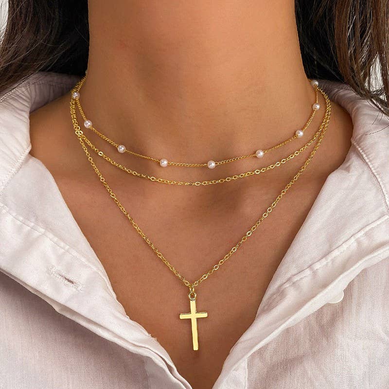 Gold necklaces with a cross pendant and pearl strands on a person wearing a white shirt.