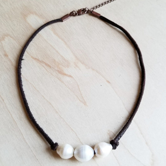 Necklace with three white beads on a dark cord against a light wooden background