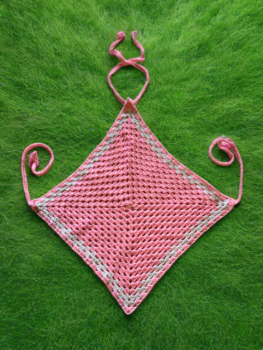 A pink crochet diamond-shaped top with adjustable straps, laid flat on a textured surface.