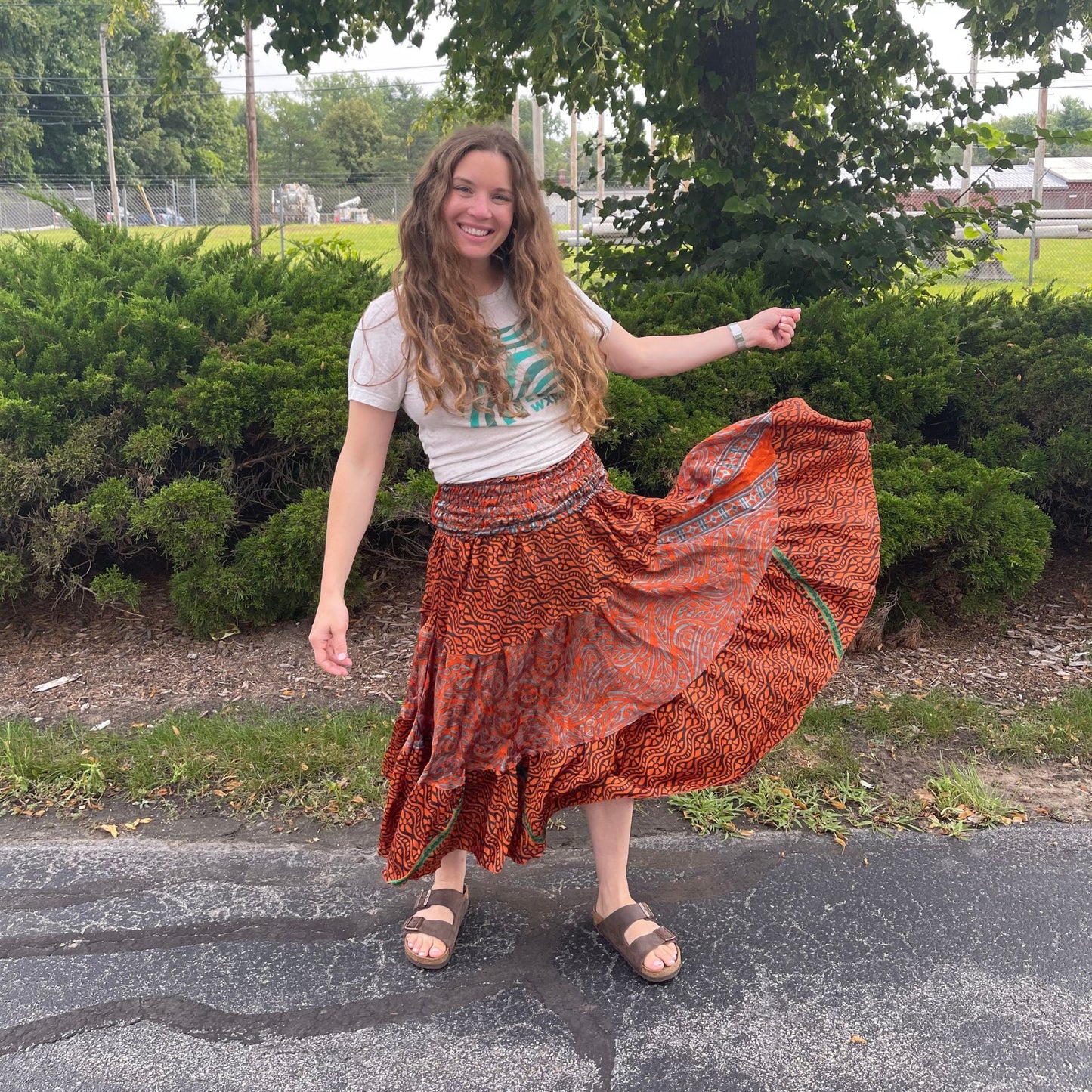 Woman in a rust-colored patterned skirt standing outdoors with greenery in the background
