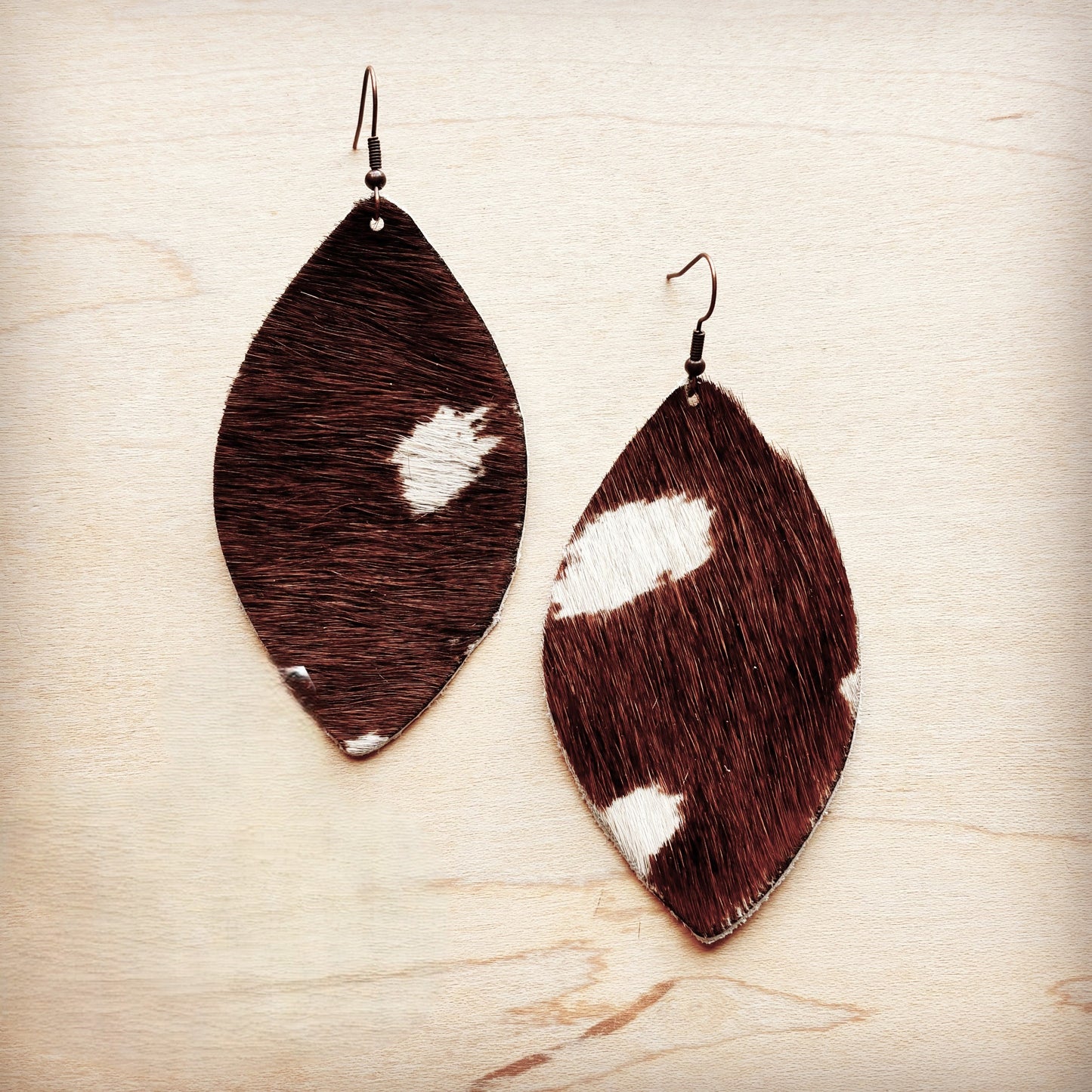 Brown and white cowhide leather earrings on a light wood background