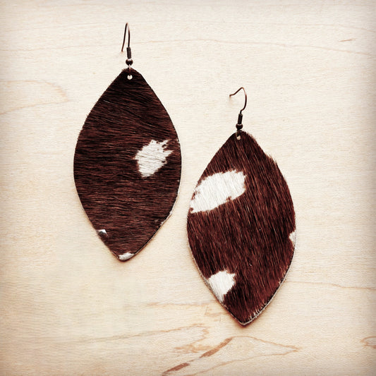 Brown and white cowhide leather earrings on a light wood background
