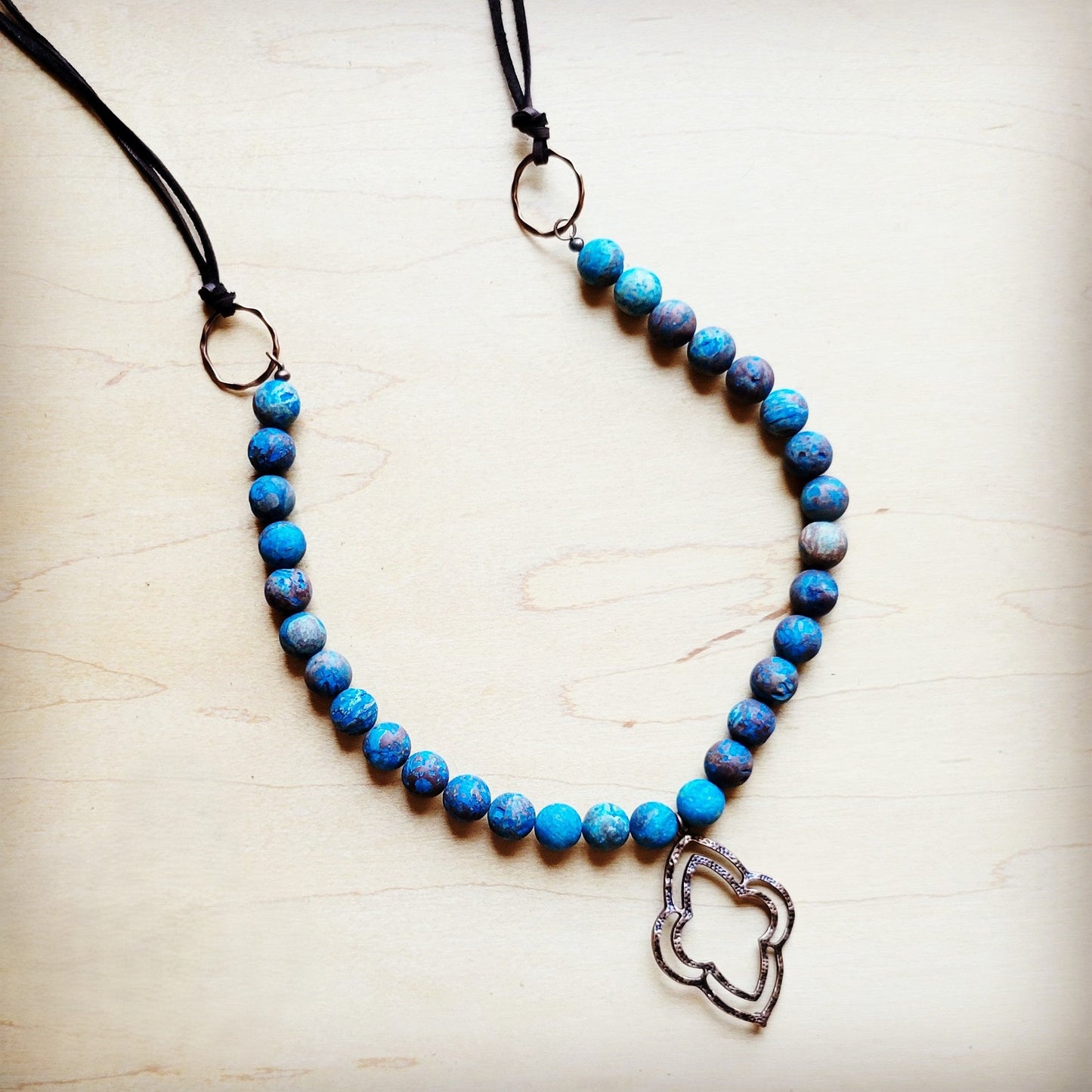 Blue beaded necklace with a silver heart pendant on a light wooden surface