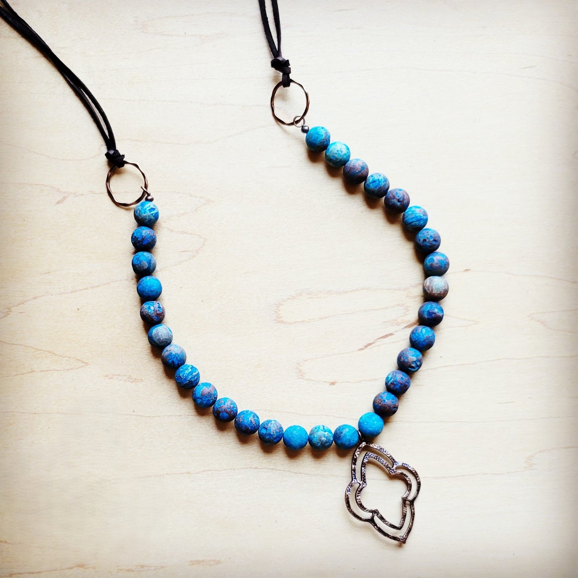 Blue beaded necklace with a silver heart pendant on a light wooden surface