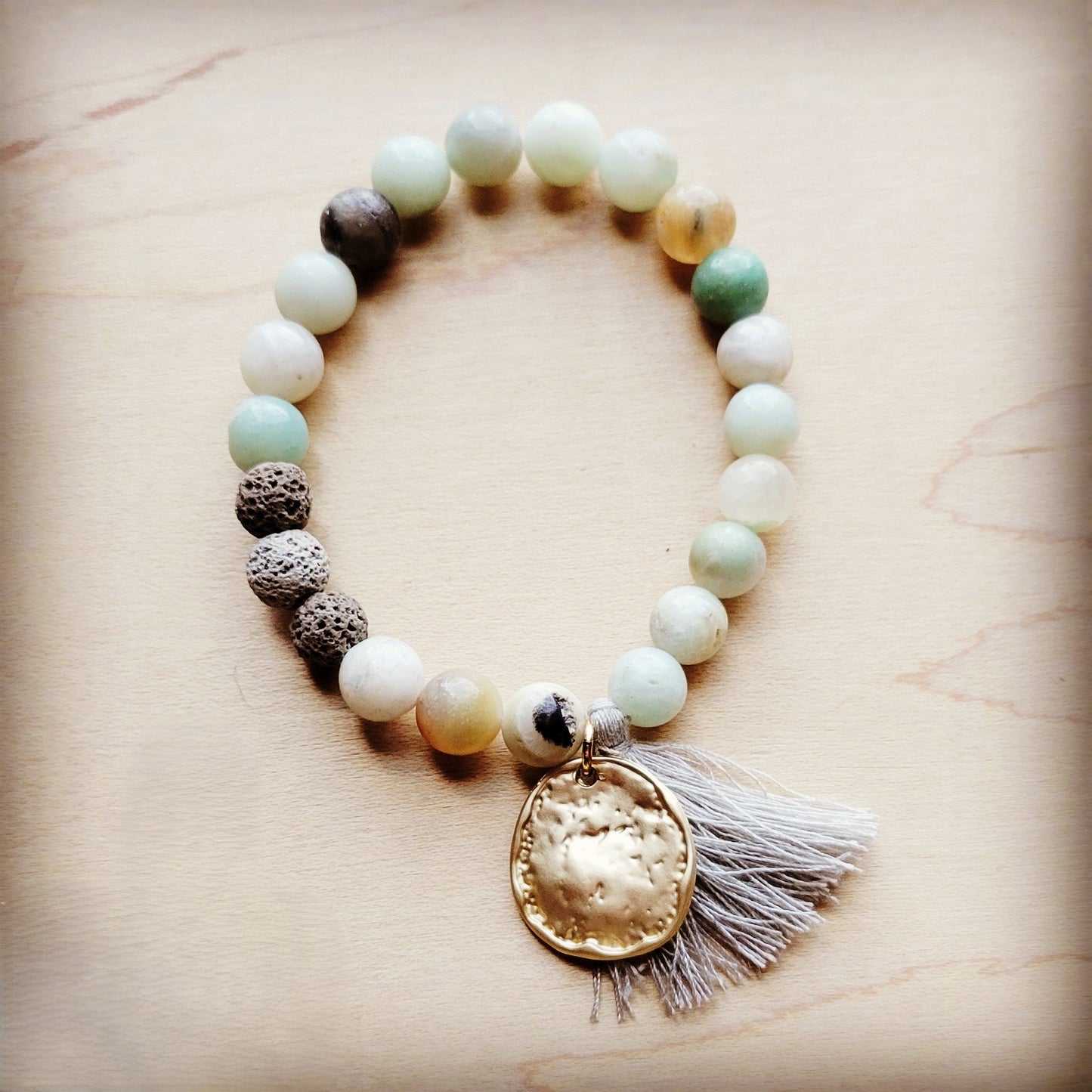 Beaded bracelet with a gold pendant and tassel on a beige background