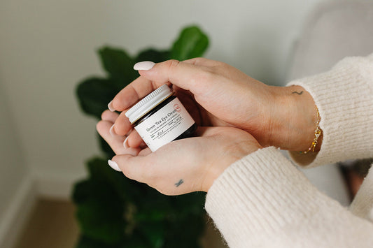Person holding a small jar of cream with a plant in the background