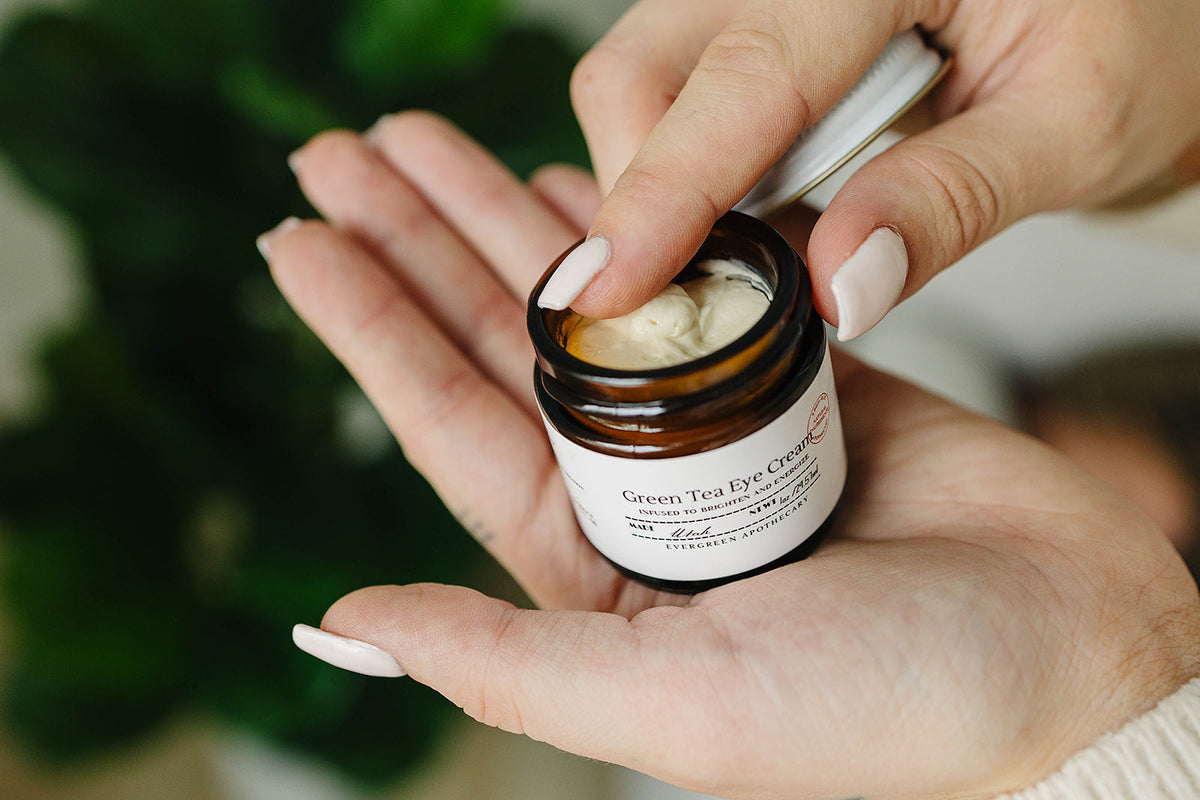 Person holding a small jar of 'Green Tea Eye Cream' with a blurred green background