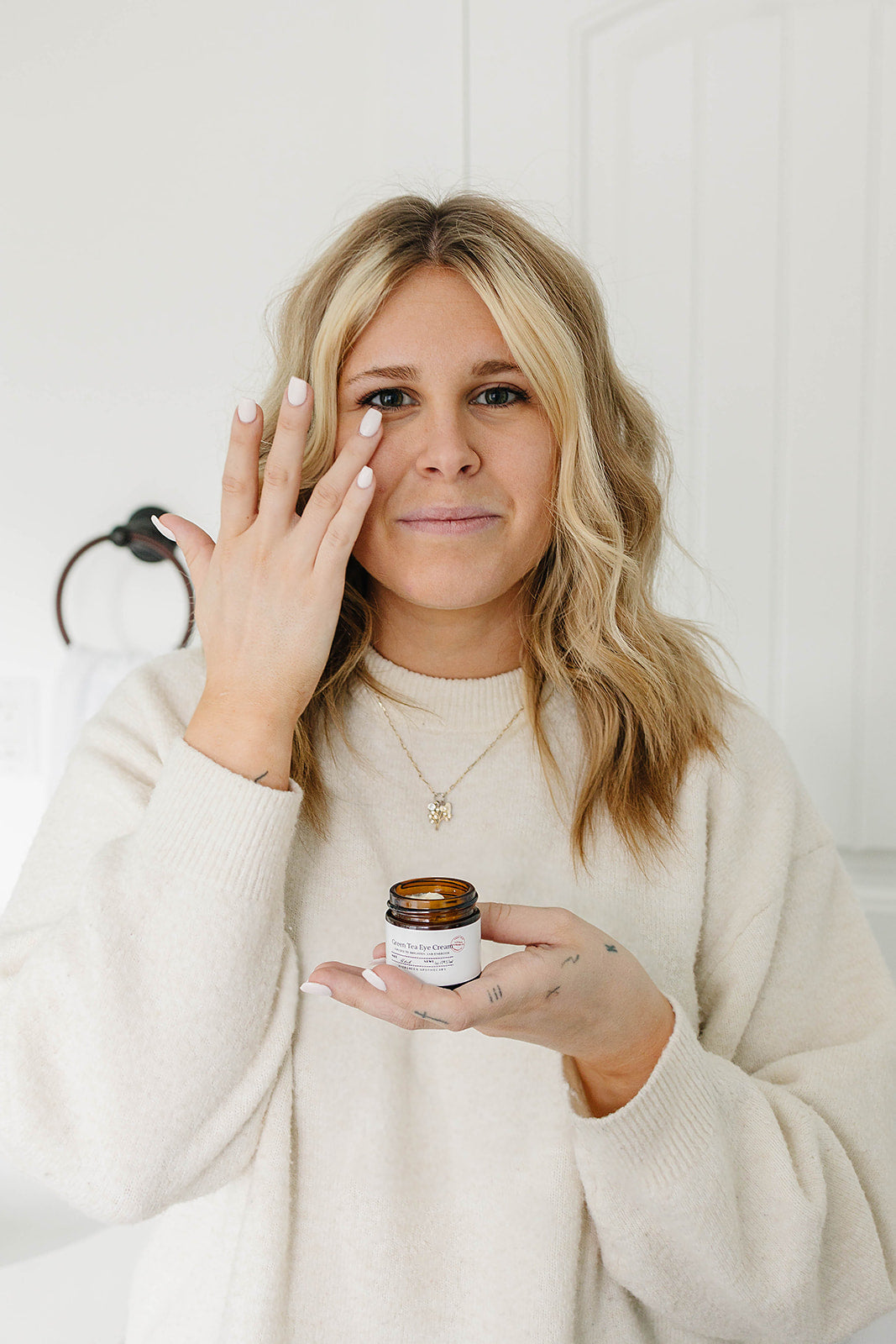 Woman holding a jar of cream and applying it to her face against a white background