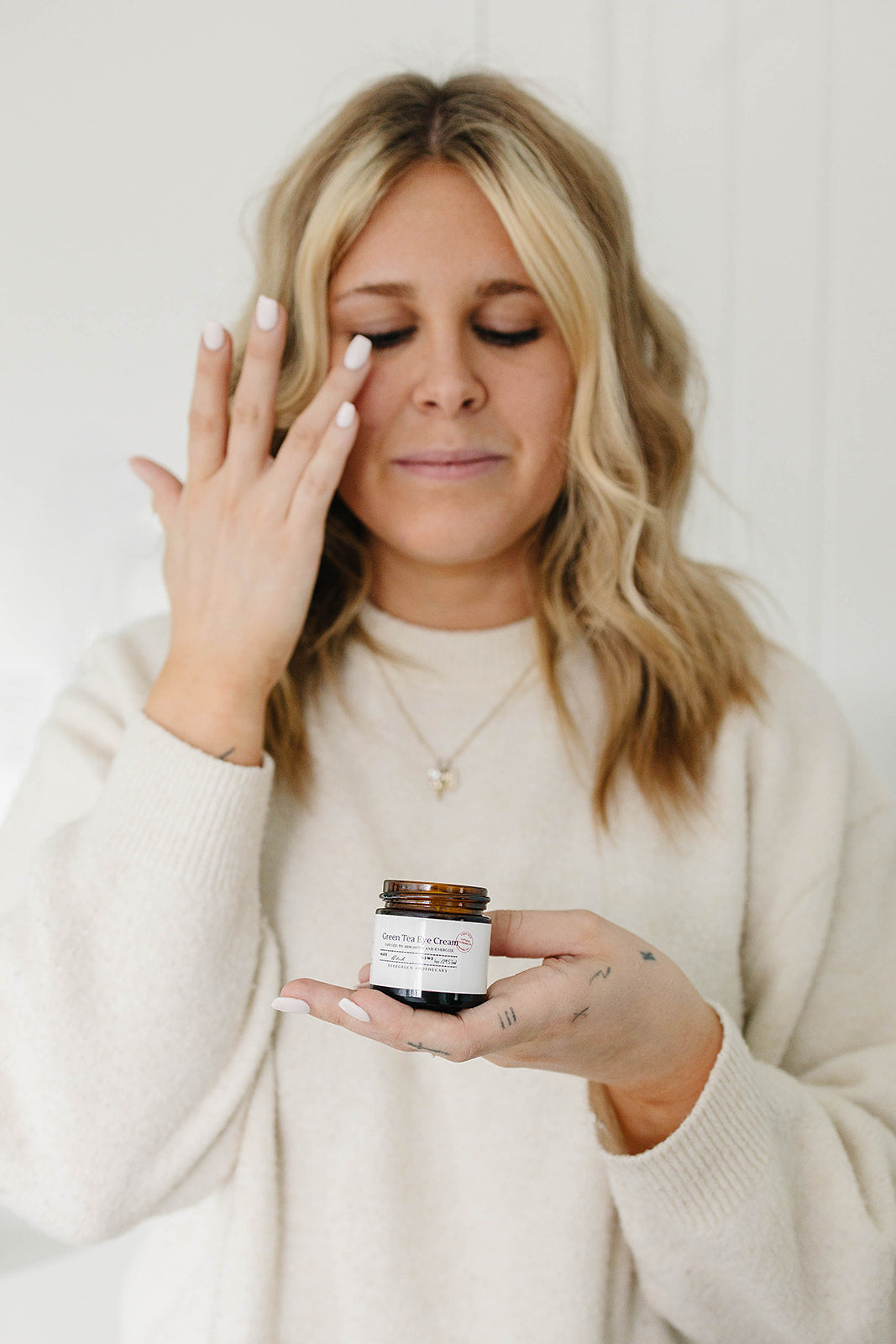 Woman applying cream to her face with a jar of the same cream in her hand.