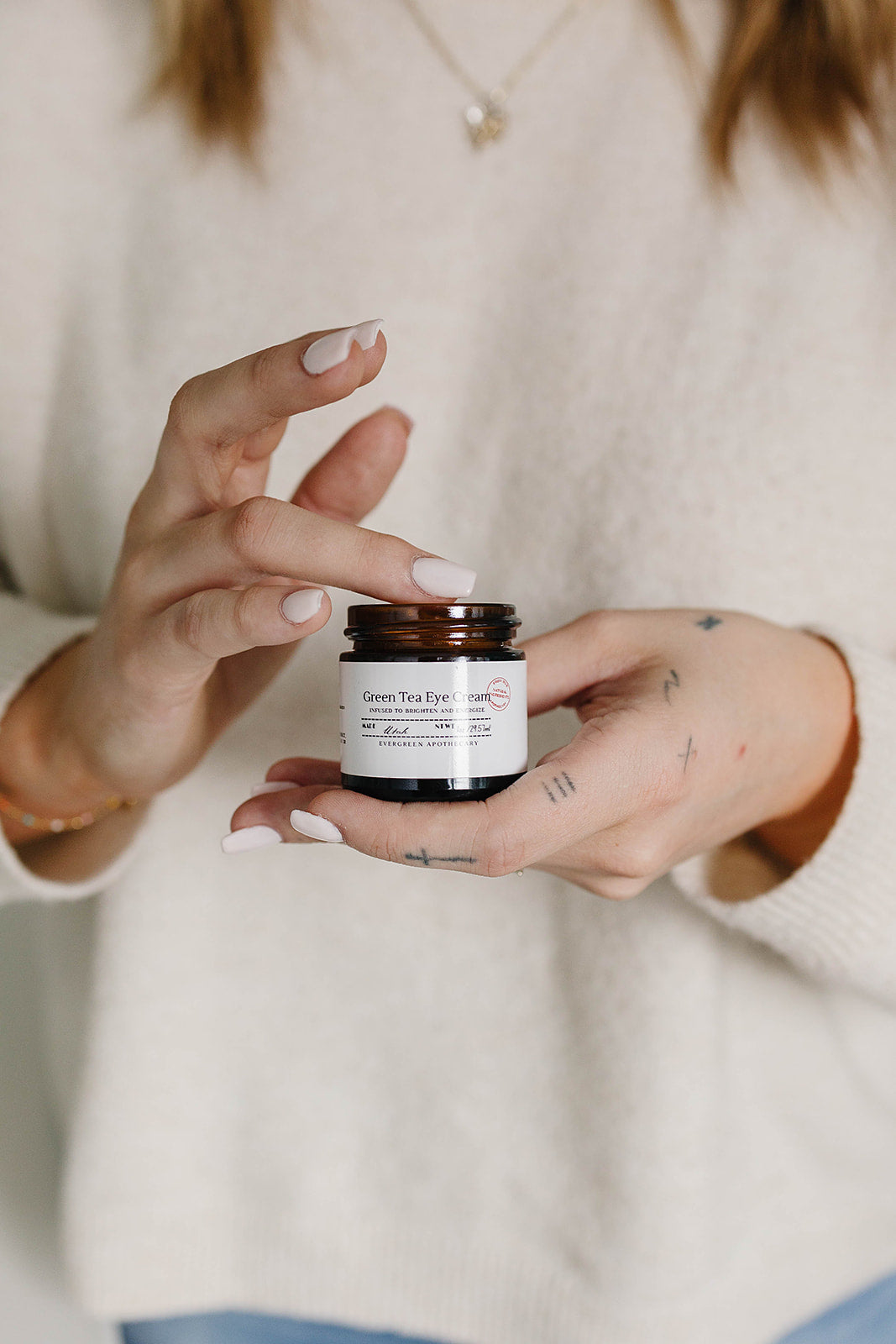 Person holding a small jar of skincare product with a neutral background