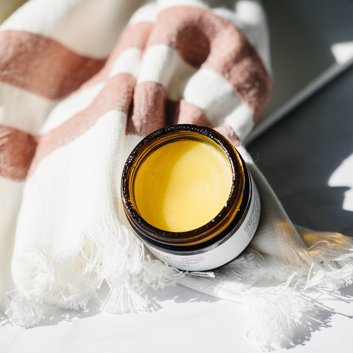 Jar of yellow cream on a checkered brown and white blanket.