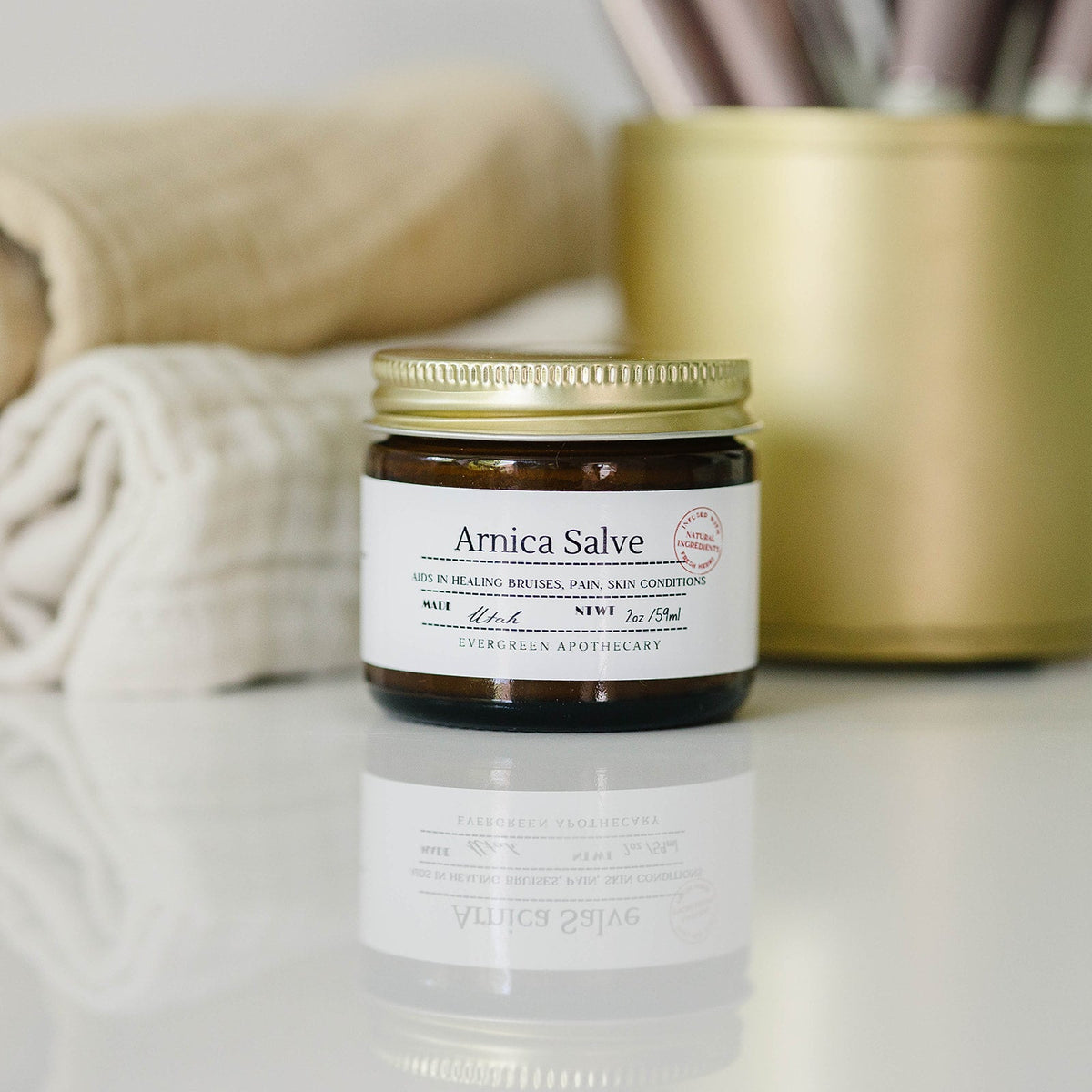 Jar of Arnica Salve on a reflective surface with a blurred background