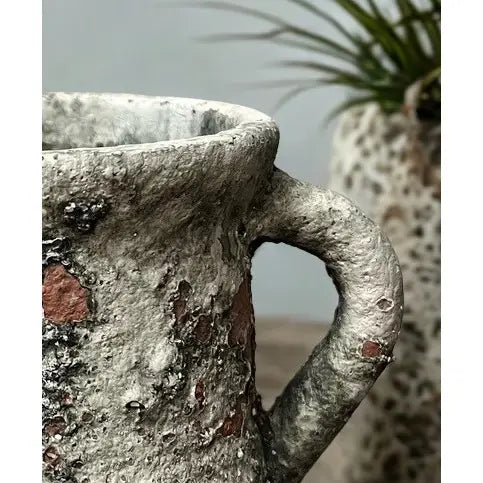 Close-up of a rustic stone planter with a handle, blurred plant in the background.