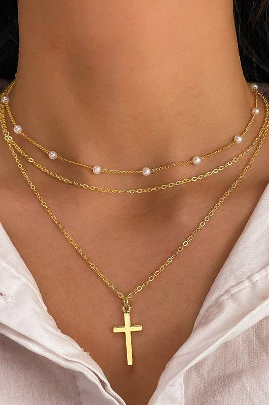 Gold necklace with a cross pendant on a person wearing a white shirt.