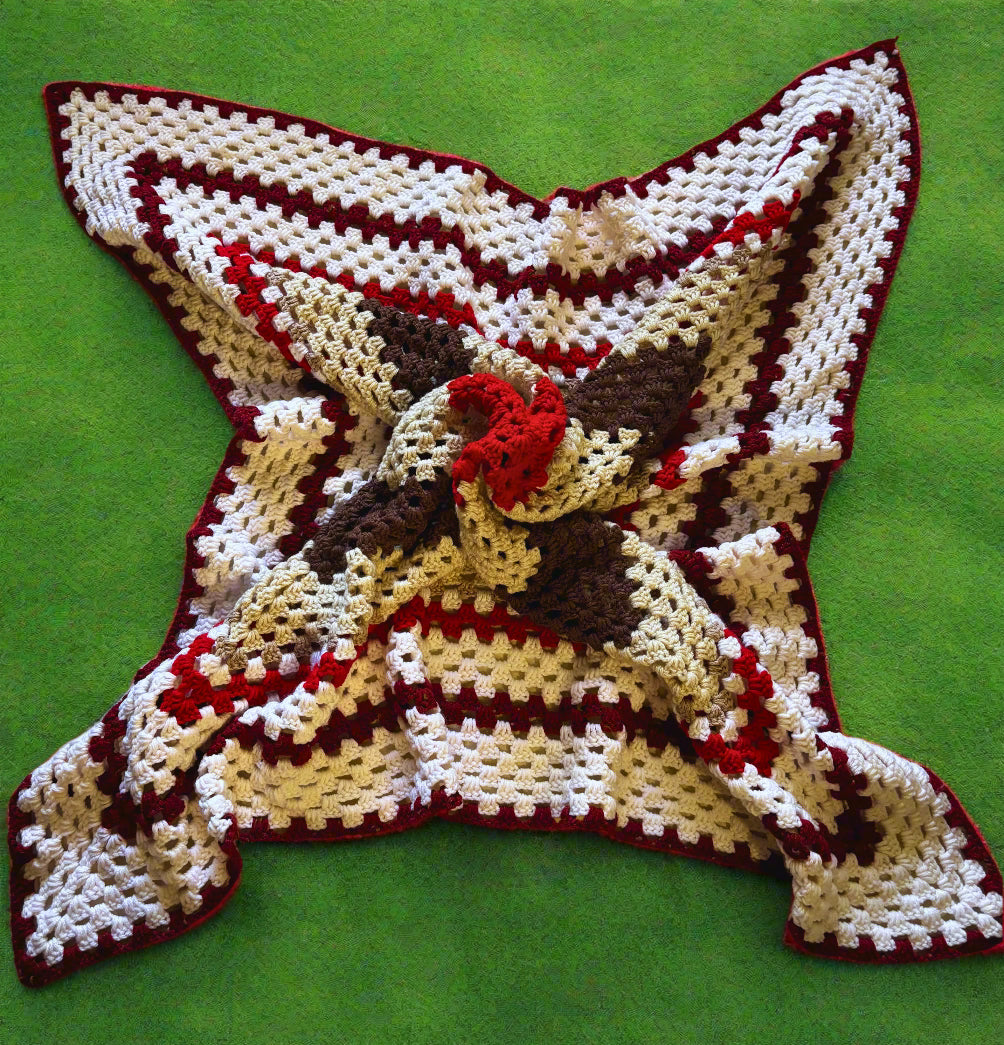 A handmade crochet afghan with a geometric pattern in red, white, and brown colors laid out on a flat surface.
