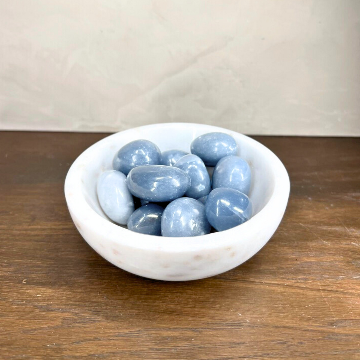 White bowl filled with blue stones on a wooden surface with a white background