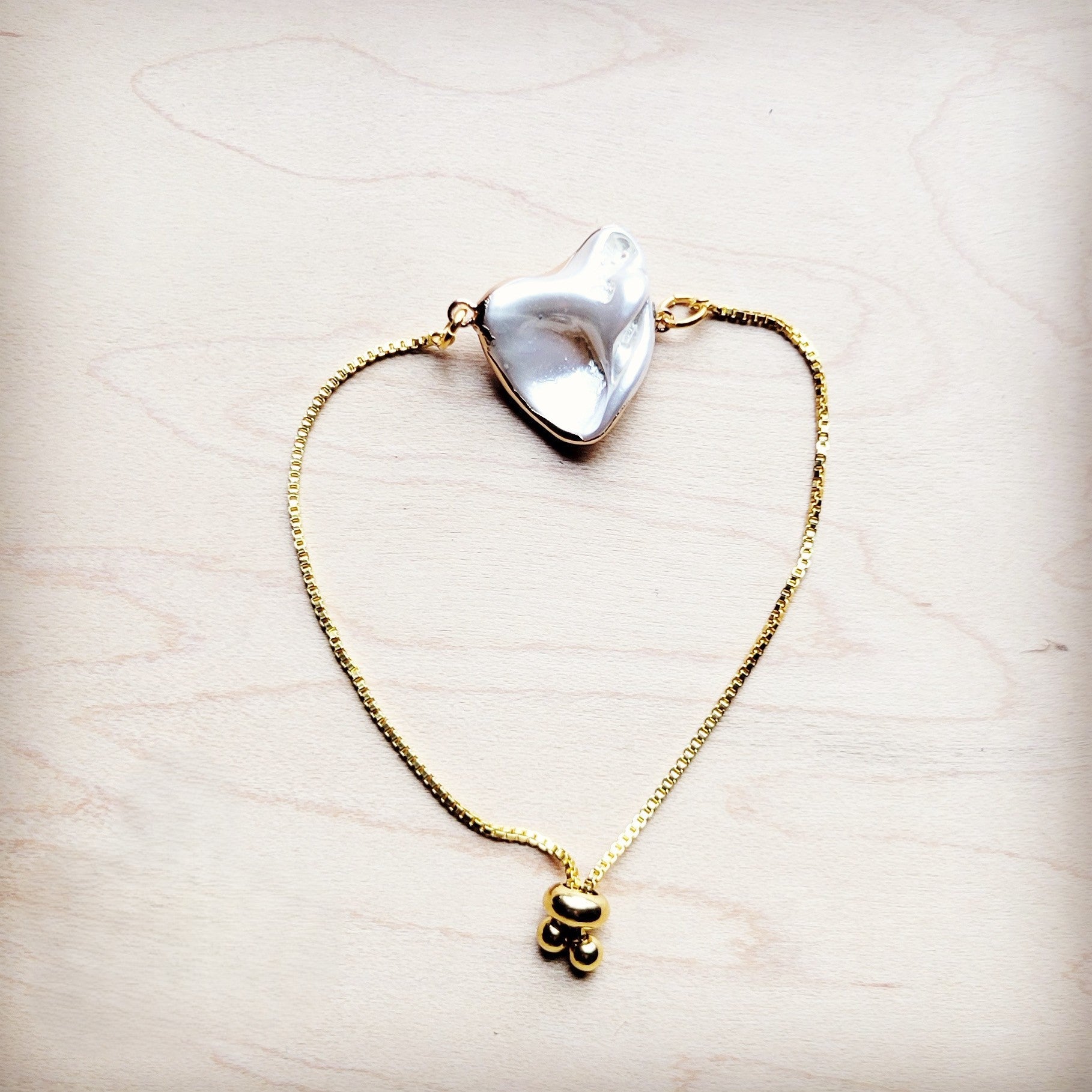 Gold necklace with a large shell pendant on a light wooden surface
