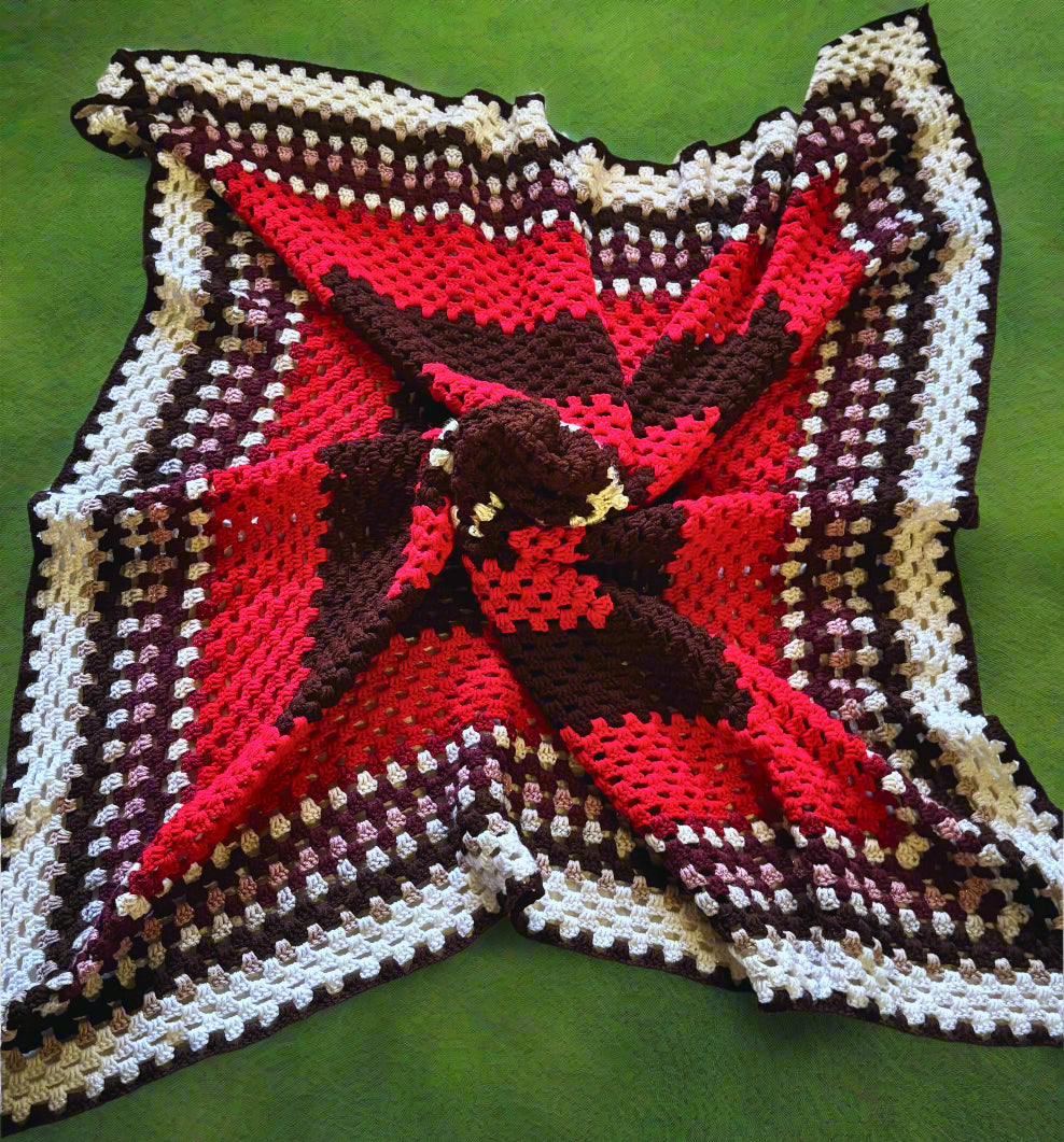 A handmade crochet afghan with a geometric pattern in red, white, and brown colors laid out on a flat surface.
