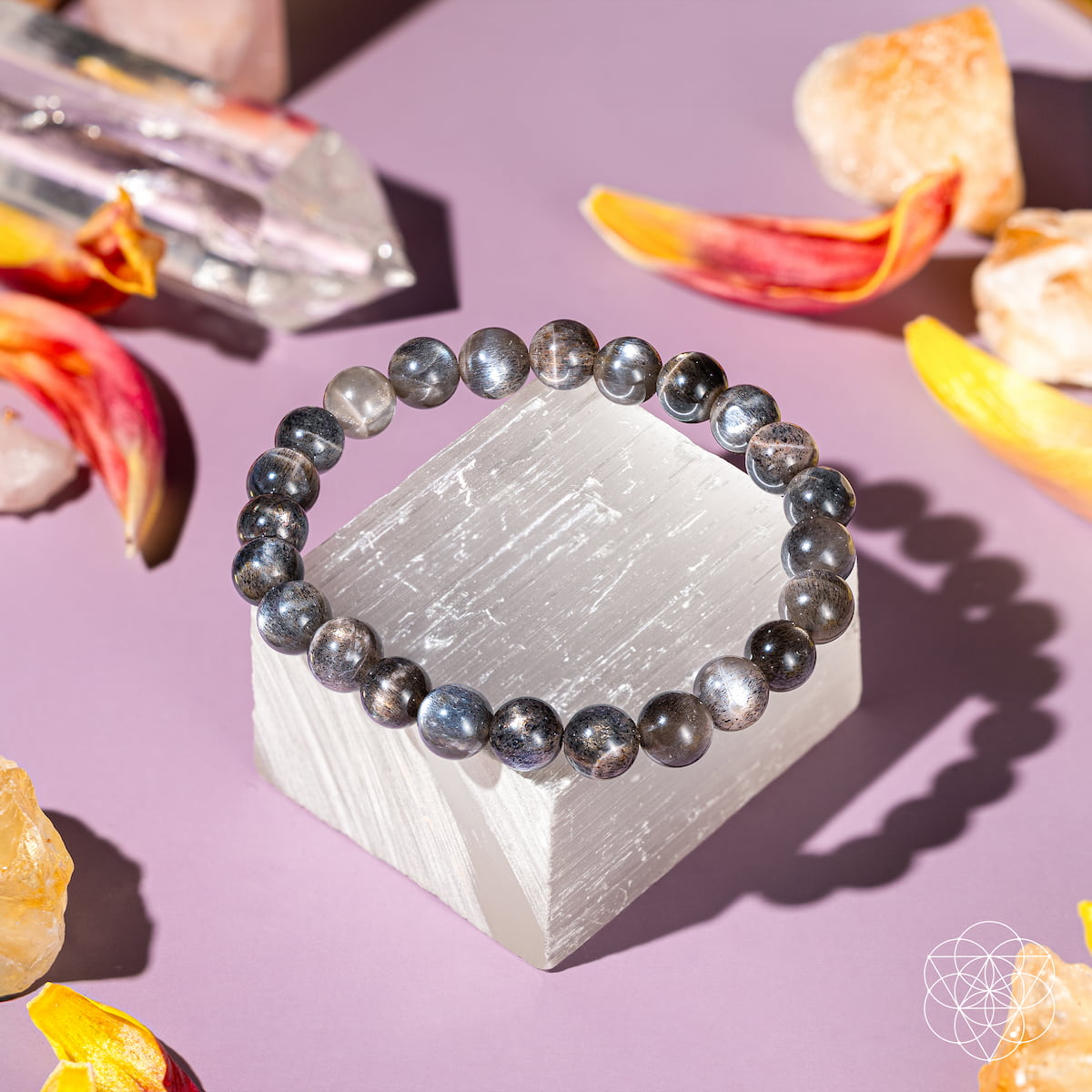 Black beaded bracelet on a crystal with crystals and flowers on a pink background