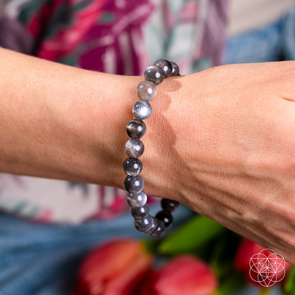 Person wearing a gray beaded bracelet on a blurred floral background