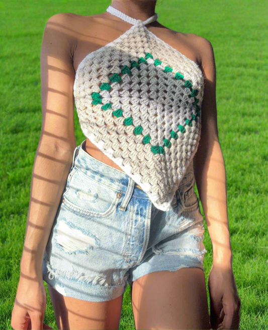 A person wearing a beige and green diamond patterned crochet top with adjustable straps, paired with denim shorts.