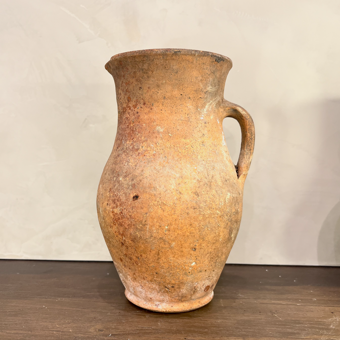 Vintage terracotta pitcher on a wooden surface with a plain background