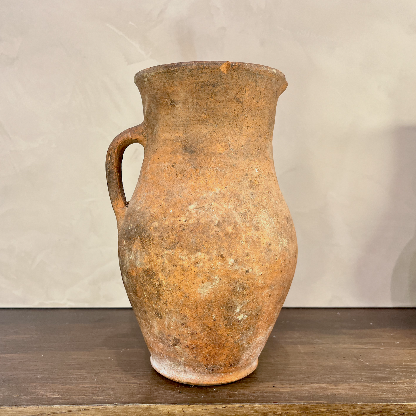 Vintage terracotta pitcher on a wooden surface with a neutral background