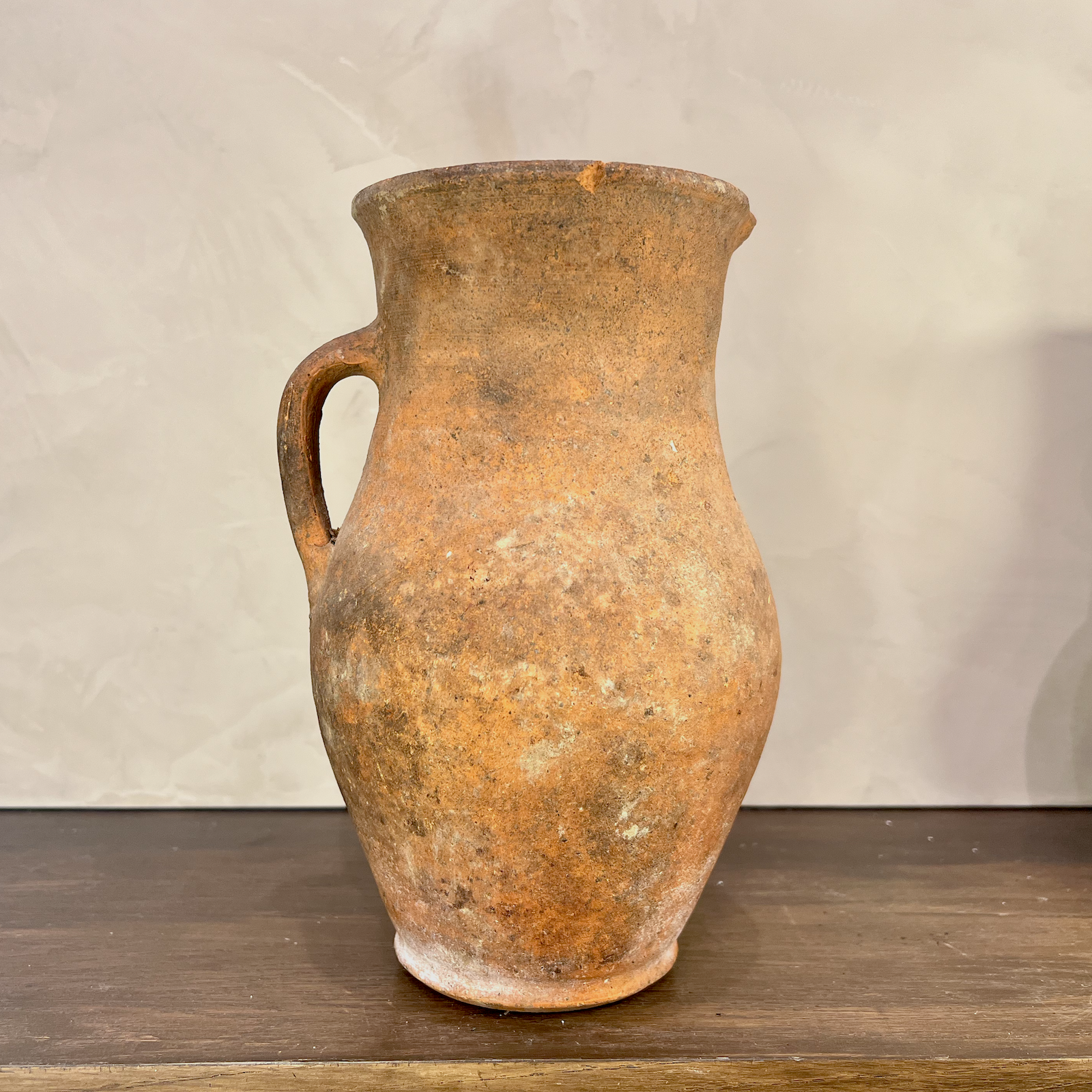 Vintage terracotta pitcher on a wooden surface with a neutral background