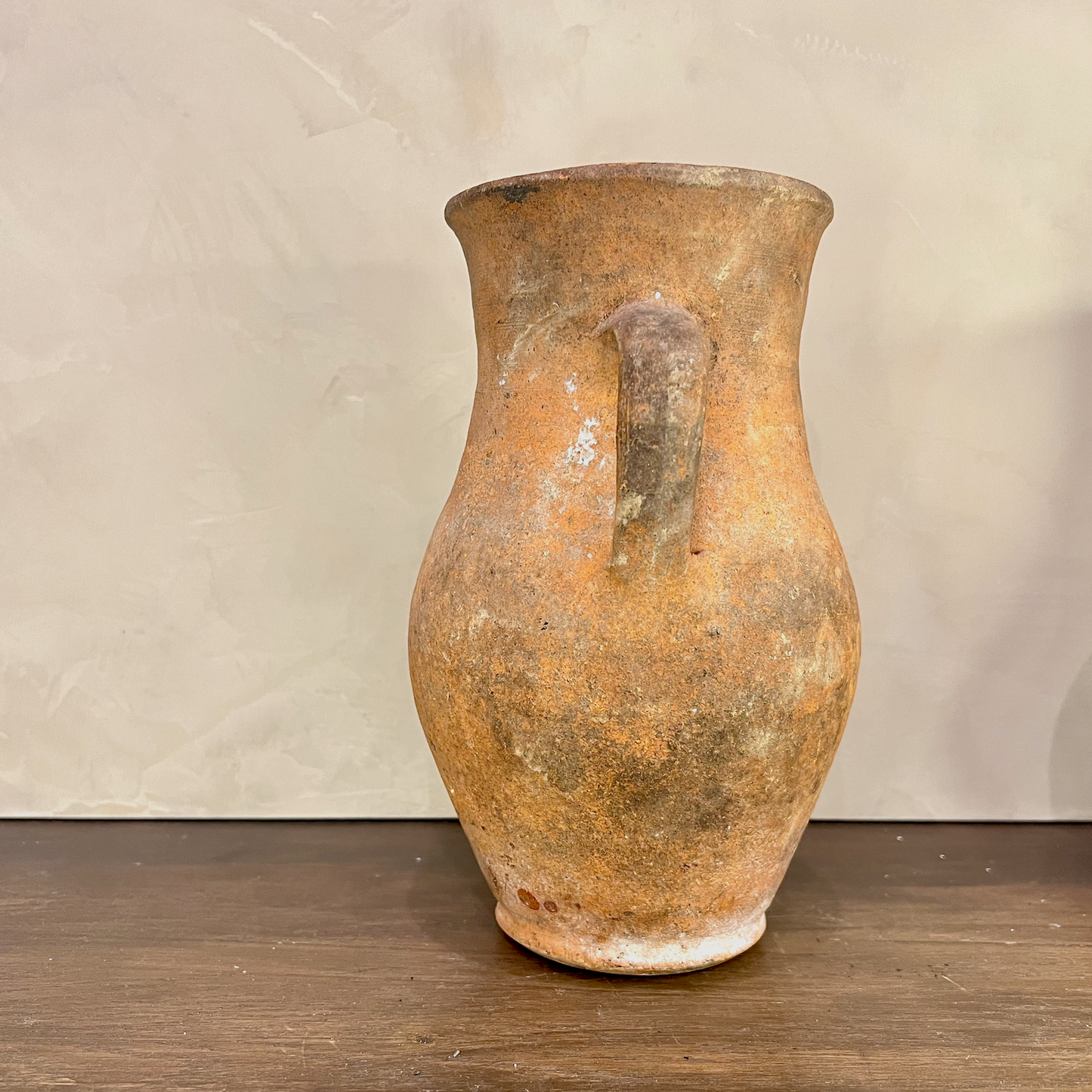 Vintage terracotta pitcher on a wooden surface with a neutral background