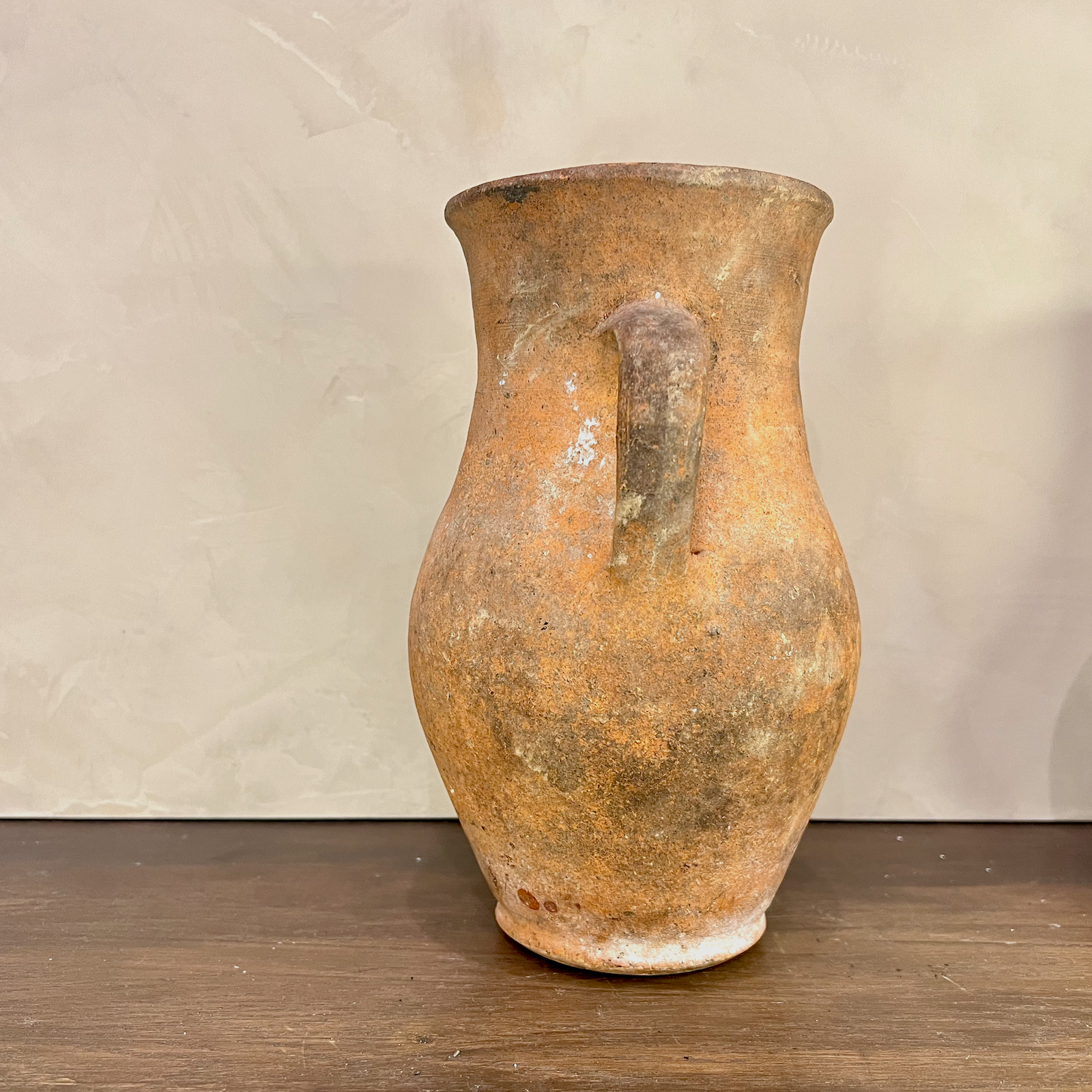 Vintage terracotta pitcher on a wooden surface with a neutral background