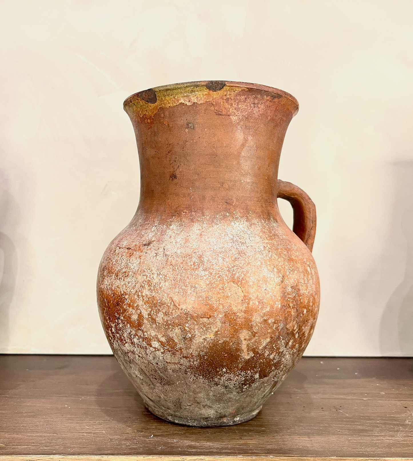 Vintage terracotta pitcher on a wooden surface with a plain background