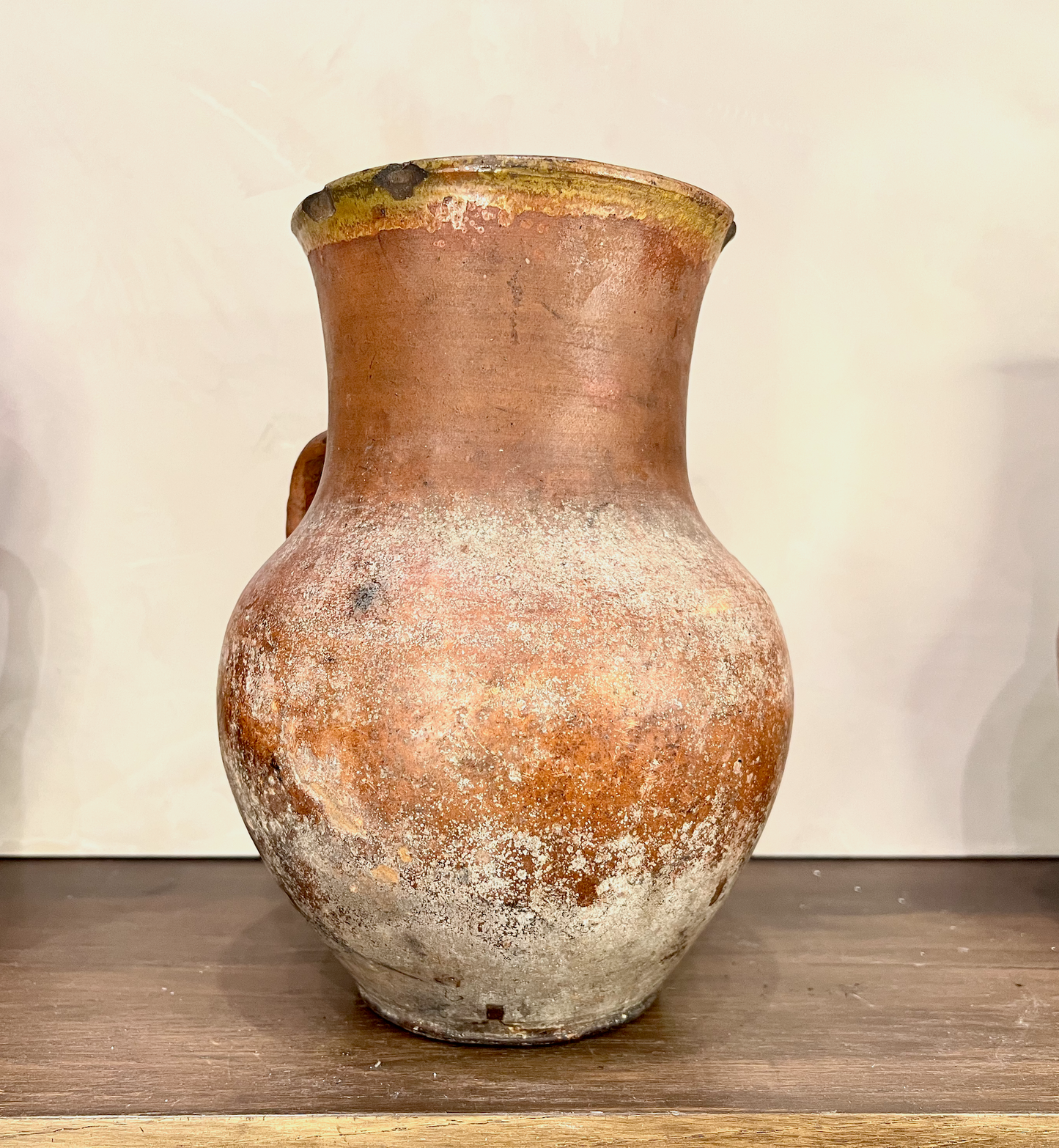 Vintage terracotta jar with a textured surface on a wooden shelf.