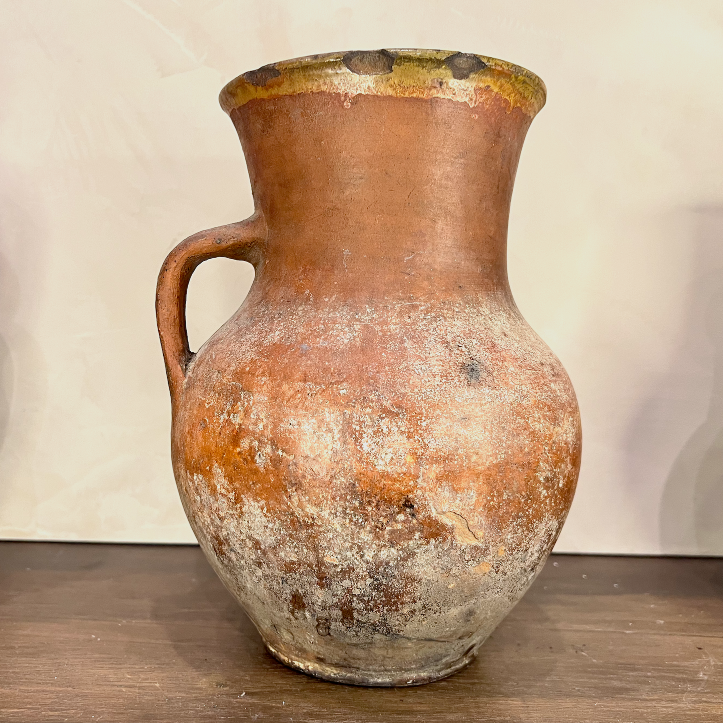 Vintage terracotta pitcher with a handle on a wooden surface and light background