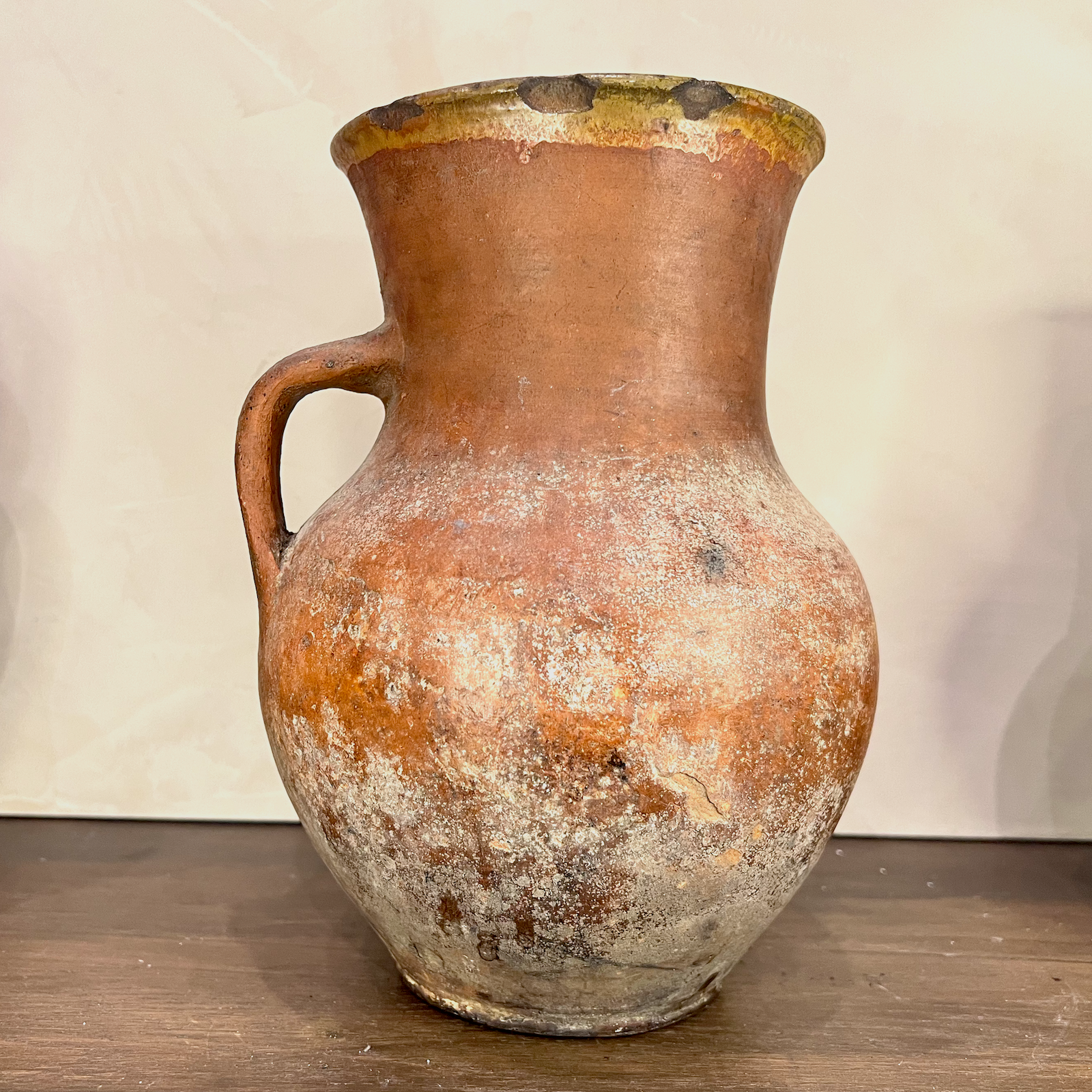 Vintage terracotta pitcher with a handle on a wooden surface and light background