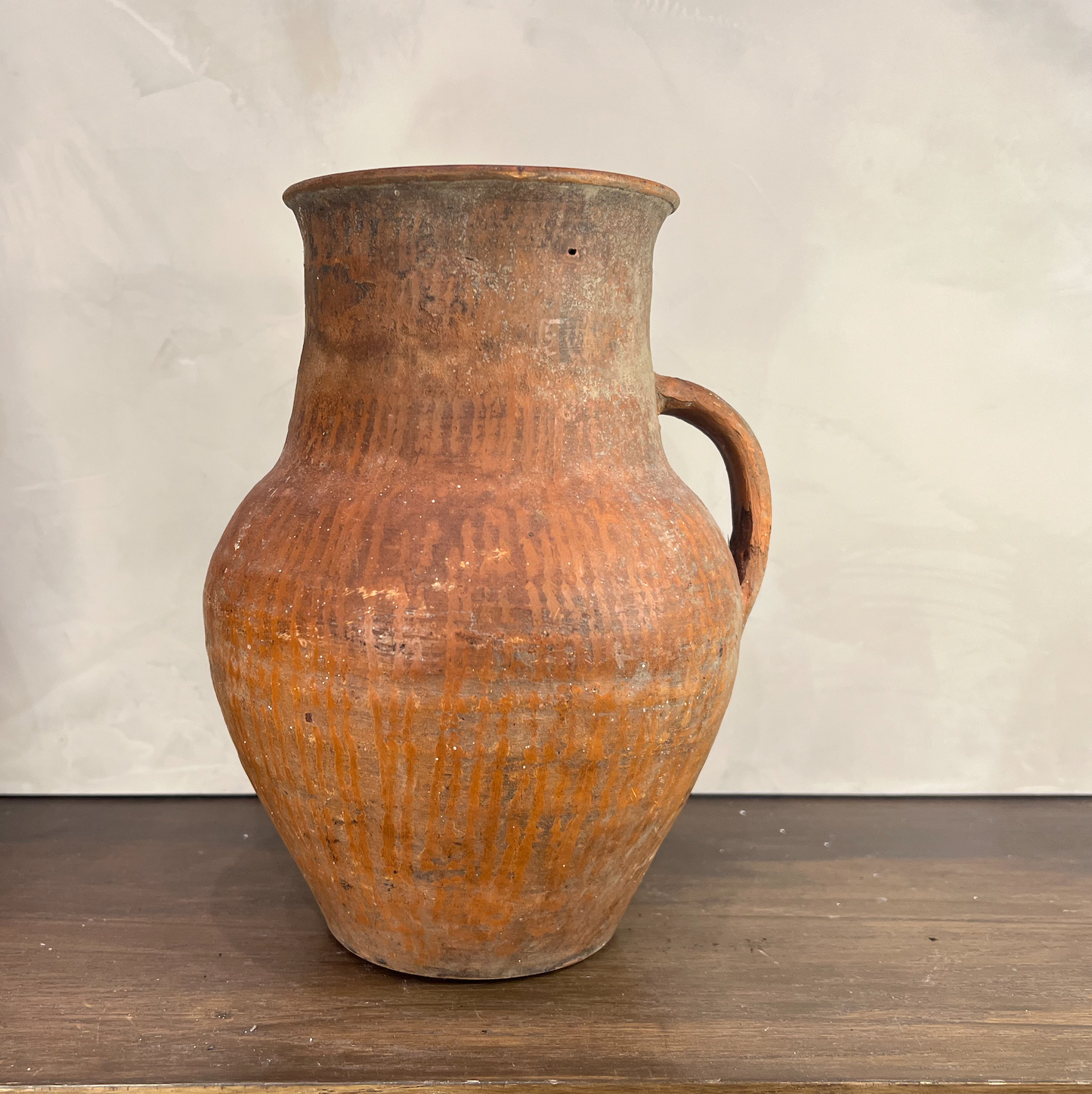 Vintage terracotta jar with a handle on a wooden surface and white background