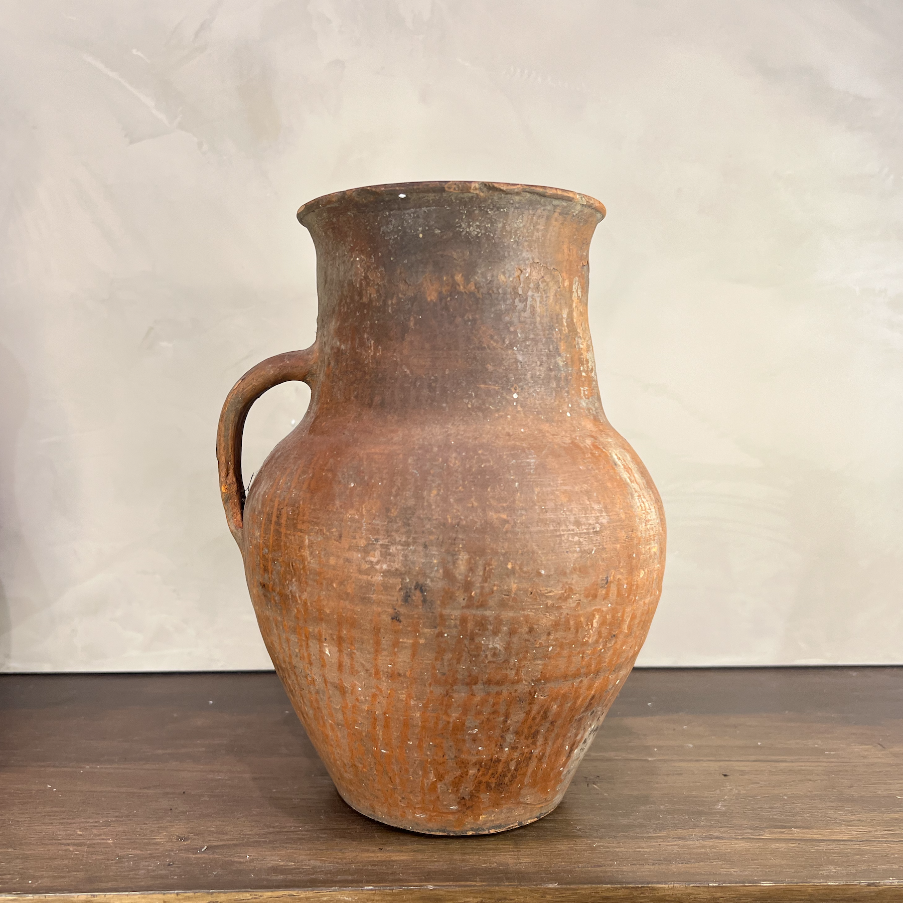 Vintage terracotta pitcher on a wooden surface with a neutral background